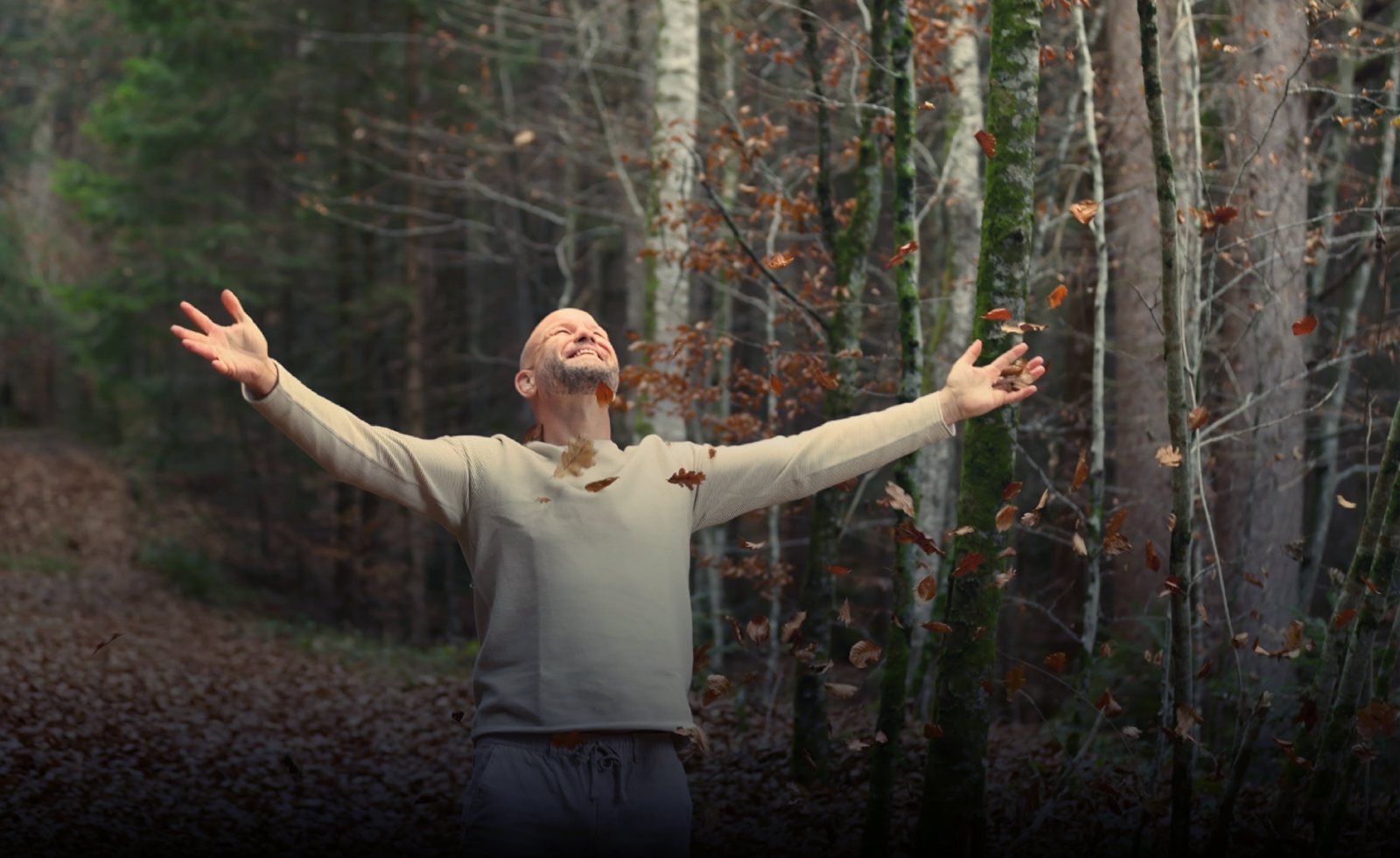 Emotionale Balance und innere Stärke: André Walberer breitet im herbstlichen Wald die Arme aus, Laub fällt um ihn herum