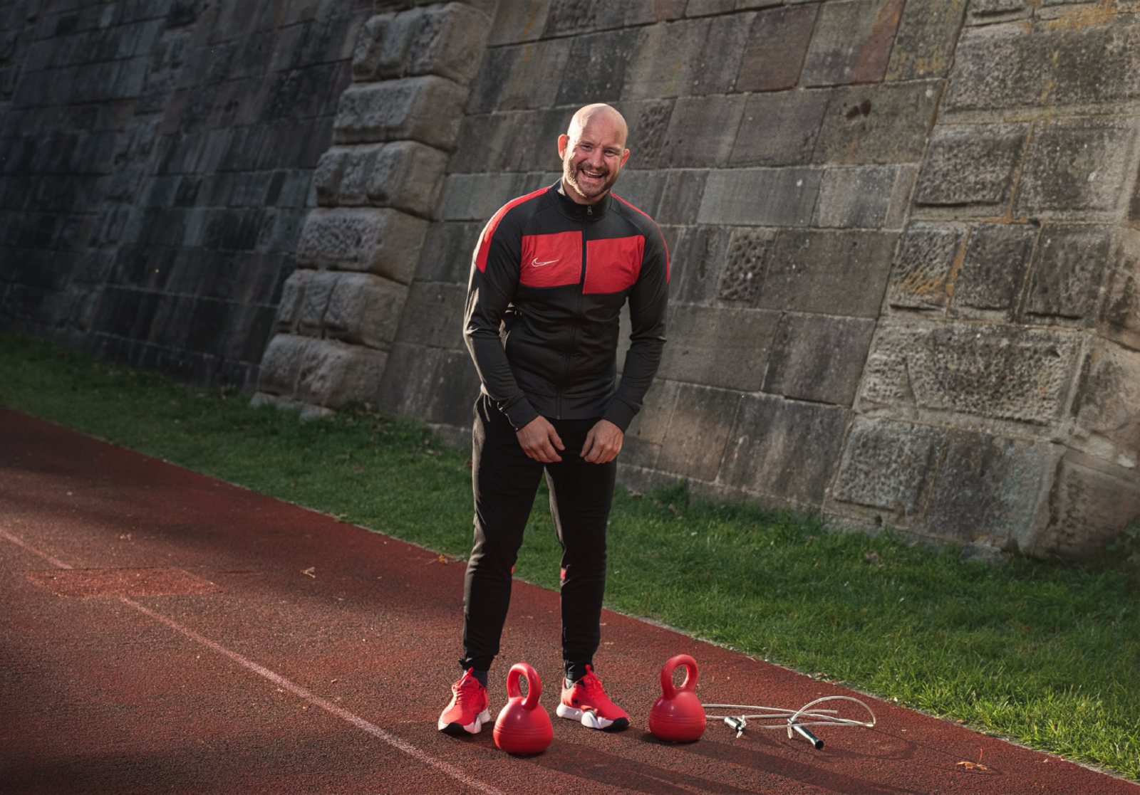 Personal Training am Wörthersee: André Walberer lacht auf der Laufbahn, vor ihm zwei rote Kettlebells und ein Springseil